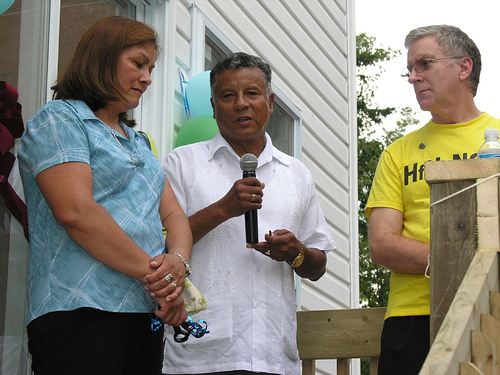 Habitat Partner Family, Carlos speaking into a microphone with Eva standing next to him during Habitat Key Ceremony for thier Habitat home.