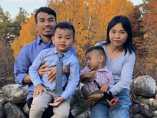 Kemptville Korners Habitat Partner Family Ceu Lian, Amang and their two children sitting outside on rocks.