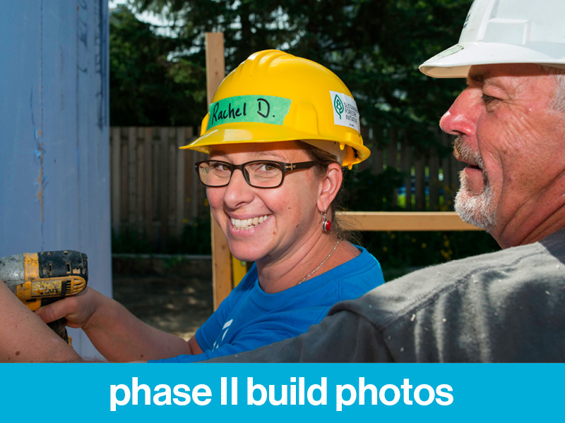 A Habitat volunteer wearing a hard hat on the Habitat build site smiling. Text at the bottom of image reads, "phase II build photos".