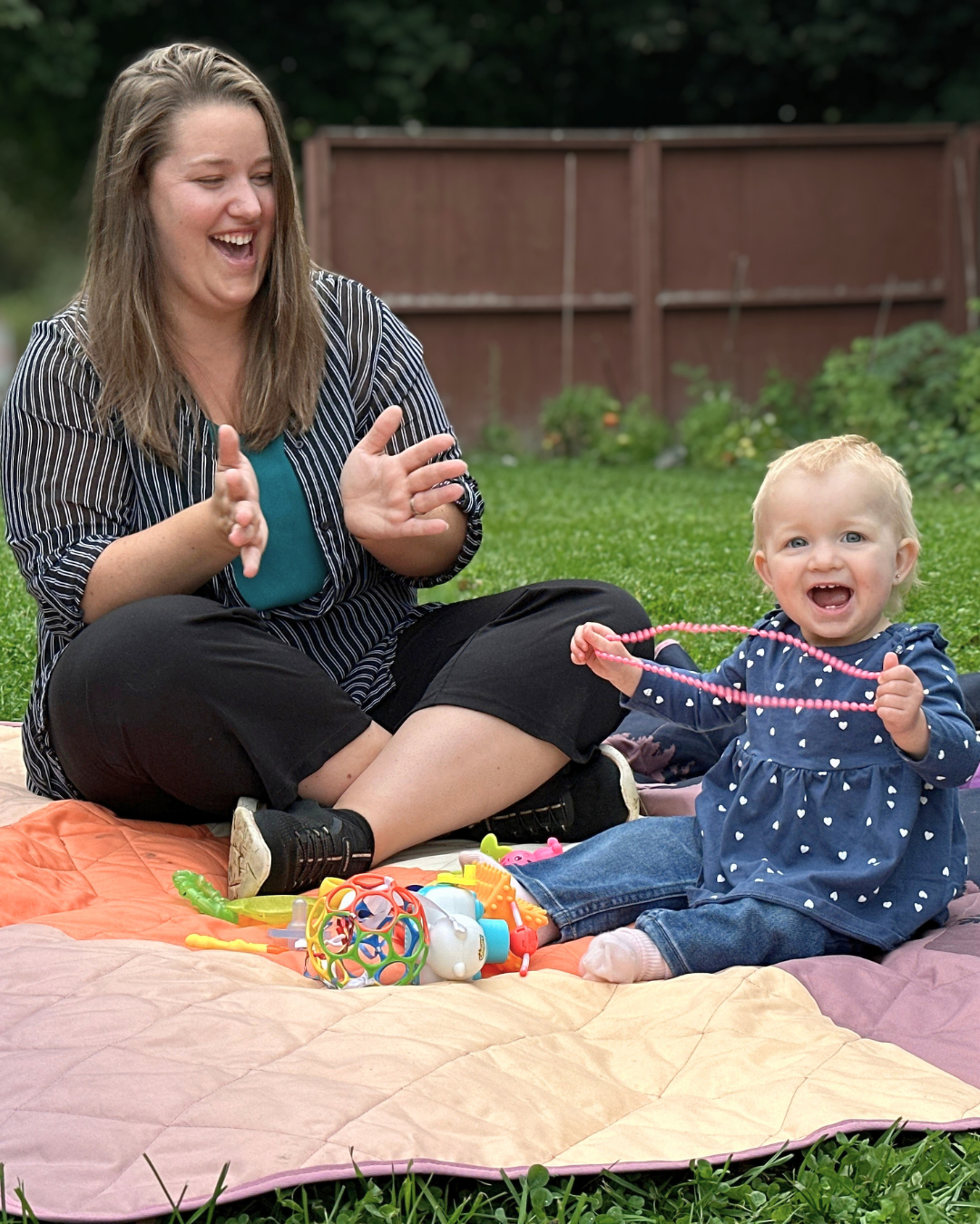 Kayla and daughter Aubrey outdoors, sitting on a picnic blanket smiling